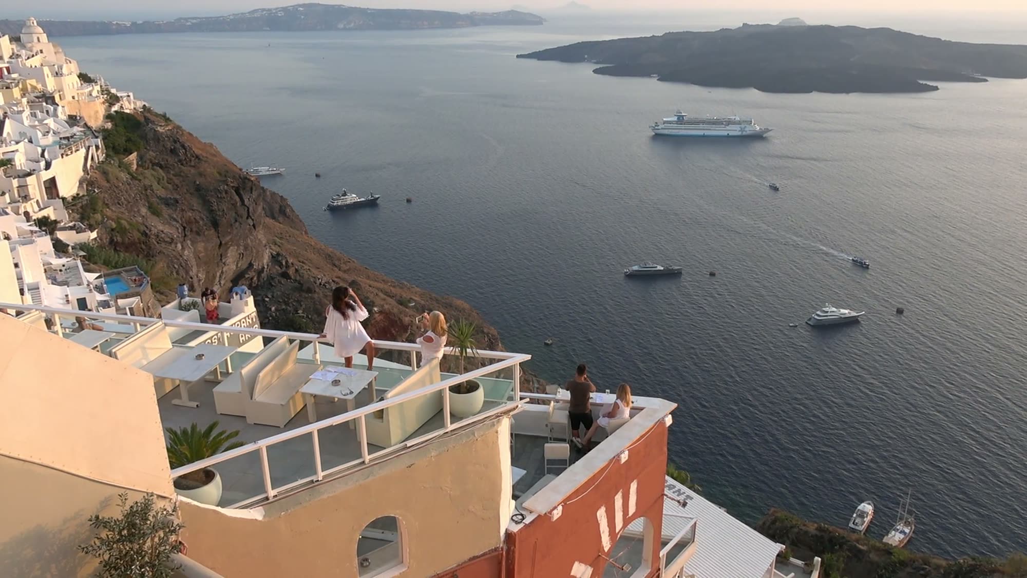 Guests on a clifftop terrace above the caldera at sunset
